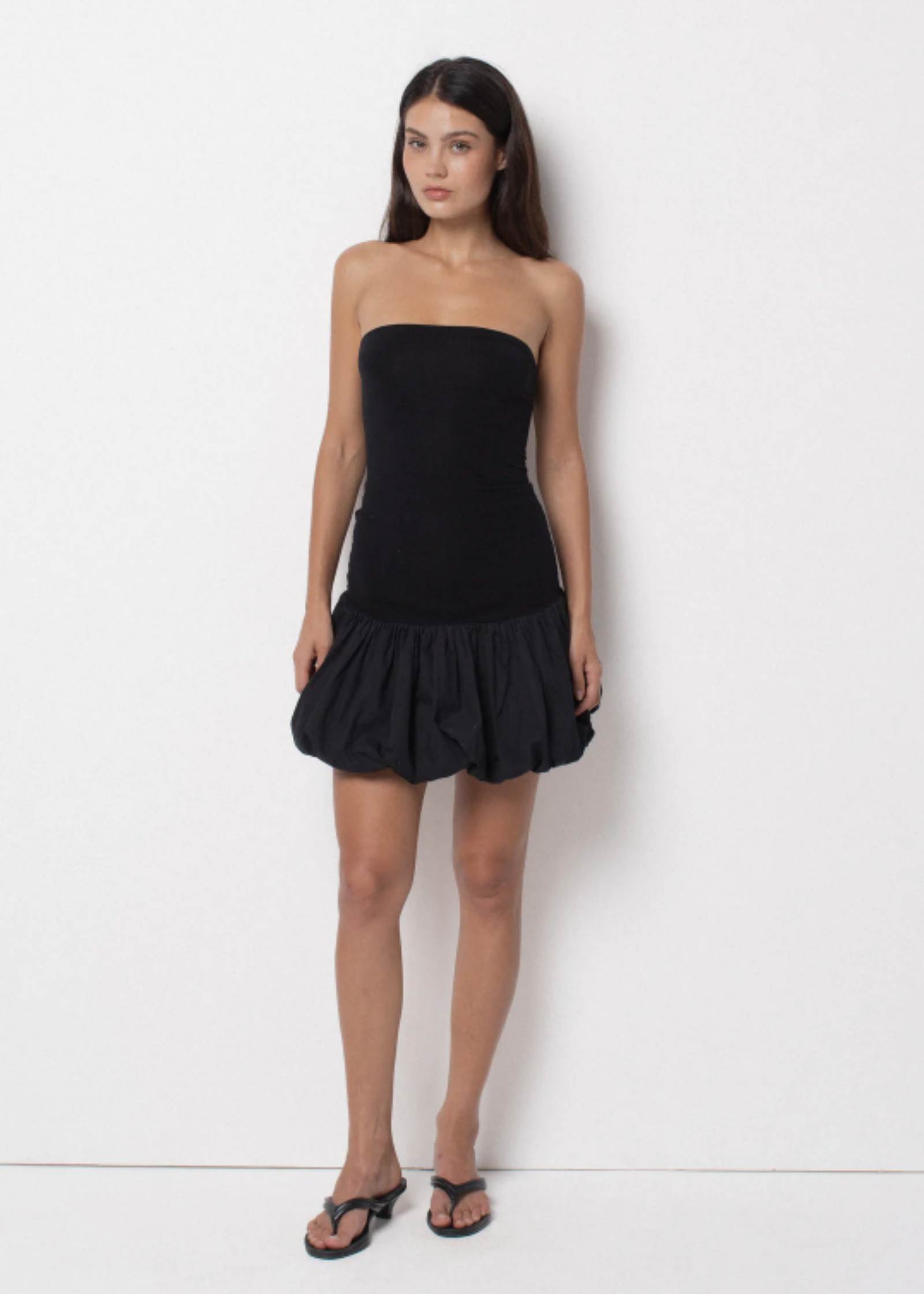 A model wearing a strapless black dress with a voluminous bubble skirt.