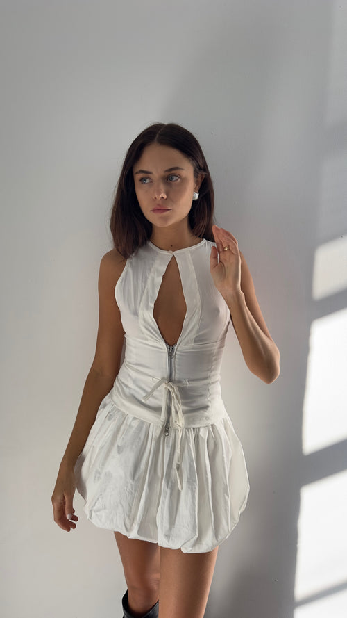 A female model wearing a cream fitted vest with semi-sheer panels, a two-way zipper, and an adjustable drawstring waist.