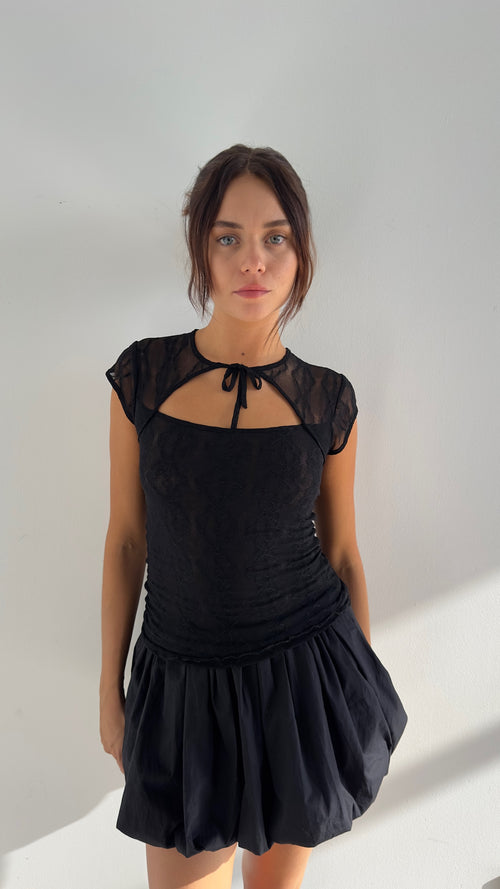 A person wearing a black mini skirt with an elastic waistband, made of lightweight cotton poplin fabric.